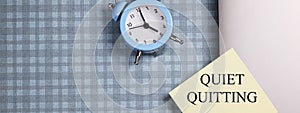 quote 'Quiet quitting' on yellow sticker on computer with clock and notebook.