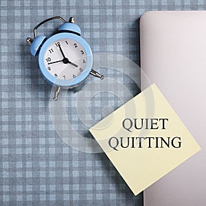 quote 'Quiet quitting' on yellow sticker on computer with clock and notebook.