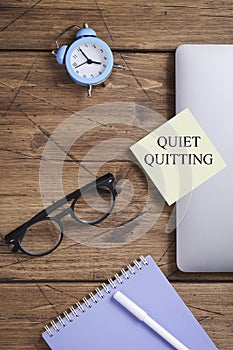 quote 'Quiet quitting' on yellow sticker on computer with clock and notebook.