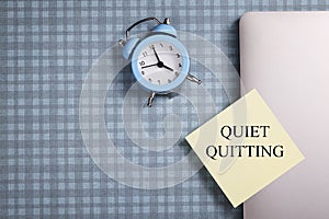 quote 'Quiet quitting' on yellow sticker on computer with clock and notebook.