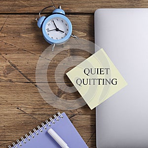 quote 'Quiet quitting' on yellow sticker on computer with clock and notebook.