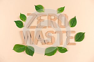 Quote ZERO WASTE made with kraft paper letters with green leaves around over light brown background