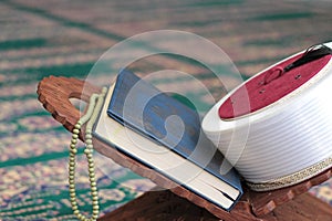 Quran, imam fez and rosary beads on a wooden stand in mosque.