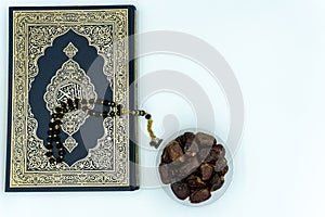 Quran with prayer beads and dates over white background