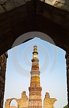 Qutub Minar and other ruins clicked from the entrance of a ruined gate. Vertical shot.