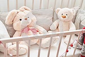 Rabbit and bear in white crib.Soft toys in children`s bedroom. White kids room.