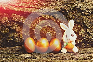 Rabbit toy, golden easter eggs on tree bark background