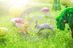 Rabbit toys with easter eggs on a meadow grass. Yellow easter egg spring meadow with two rabbit and easter eggs. Fairy