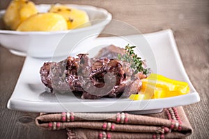 Rabbit in winy sauce with potato on a white plate.
