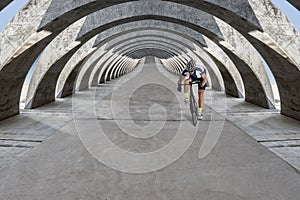 Race biker approaches under concrete arcades