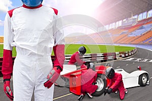 Race car driver posing in front of the pit stop with team maintaining technical service for a racing car during competition event