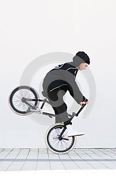 Racer makes a trick in against the background of a white wall. Bmx rider with a bicycle in flight on a white background