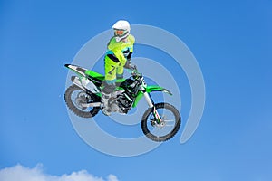 Racer on a motorcycle in flight, jumps and takes off on a springboard against the blue sky, in the frame drones do