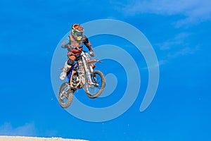 Racer on a motorcycle in flight, jumps and takes off on a springboard against the sky.