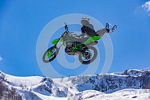 Racer on a motorcycle in flight, jumps and takes off on a springboard against the snowy mountains