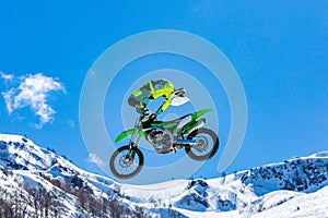 Racer on a motorcycle in flight, jumps and takes off on a springboard against the snowy mountains