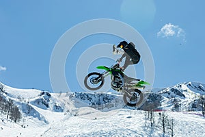 Racer on a motorcycle in flight, jumps and takes off on a springboard against the snowy mountains