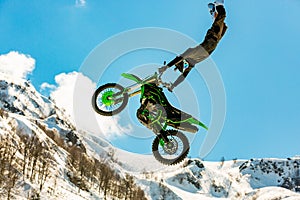 Racer on a motorcycle in flight, jumps and takes off on a springboard against the snowy mountains