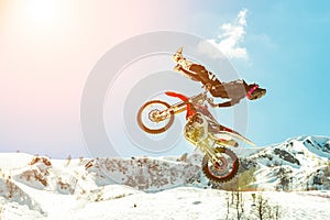 Racer on a motorcycle in flight, jumps and takes off on a springboard against the snowy mountains