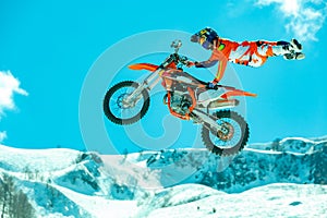 Racer on a motorcycle in flight, jumps and takes off on a springboard against the snowy mountains