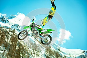 Racer on a motorcycle in flight, jumps and takes off on a springboard against the snowy mountains