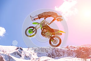 Racer on a motorcycle in flight, jumps and takes off on a springboard against the snowy mountains