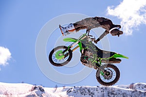 Racer on a motorcycle in flight, jumps and takes off on a springboard against the snowy mountains