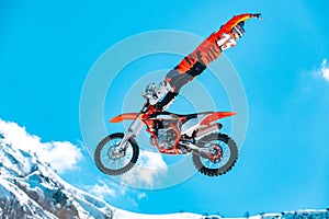 Racer on a motorcycle in flight, jumps and takes off on a springboard against the snowy mountains