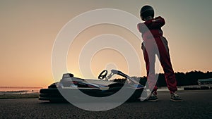 Racer in sportswear is standing next to his go-cart