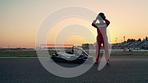 A racer is standing next to a car and puts a helmet on