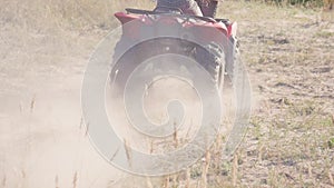 Racing ATV on the sand in summertime. A young guy in sunglasses creates a large cloud of dust and debris on sunny day