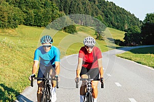 Racing cyclist couple in sports jerseys, pedaling on a road