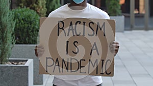 RACISM IS A PANDEMIC on cardboard poster in hands of African American male protester activist. Stop Racism concept, No