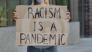 RACISM IS A PANDEMIC on a cardboard poster in the hands of female protester activist. Closeup of poster and hand. Stop