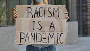 RACISM IS A PANDEMIC on cardboard poster in hands of female protester activist. Stop Racism concept, No Racism. Rallies