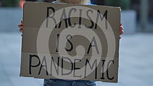 RACISM IS A PANDEMIC on cardboard poster in hands of female protester activist. Stop Racism concept, No Racism. Rallies