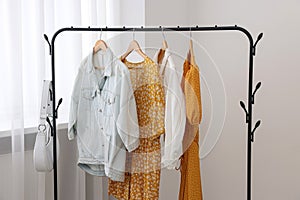 Rack with bag and stylish women's clothes on hangers near light wall indoors