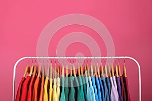 Rack with bright clothes on pink background. Rainbow colors