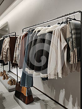 Rack with clothes on hangers and shoes in the store against the background of a small wall