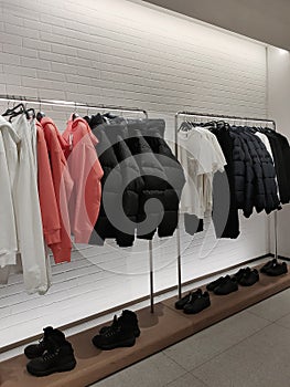 Rack with clothes on hangers and shoes in the store against the background of a small wall