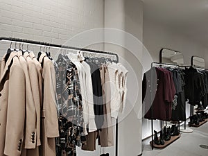 Rack with clothes on hangers and shoes in the store against the background of a small wall