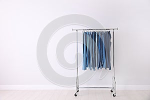 Rack with different jeans near light wall. Space for text