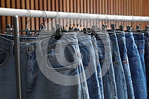 Rack with different jeans on wooden background, closeup