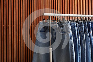 Rack with different jeans on wooden background. Space for text