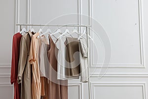 Rack with different stylish women`s clothes near white wall indoors, space for text