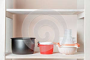 A rack with dishes in a warehouse close-up, a black saucepan, a red ladle and drainage sieves for cheese making