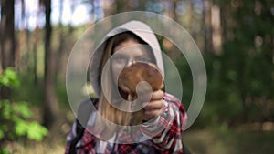 Rack focus from beautiful smiling woman to mushroom in female Caucasian hand. Confident young gatherer picking fungi in