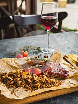 Rack of grilled ribs, buckwheat with mushroom and tomatoes on old wooden cutting board and glass of red vine