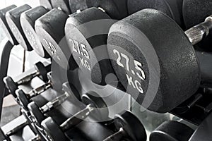 A rack of heavy dumbbells with weight labels in kilograms at the gym. Weight training equipment