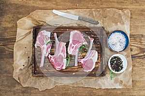 Rack of Lamb with rosemary and spices on rustic chopping board over oily craft paper, old wooden background